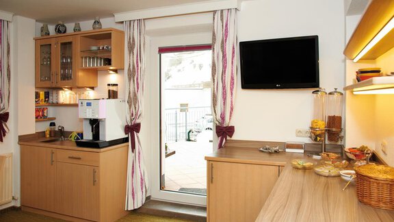 A modern kitchen with wooden furniture and a large window front. Snacks and a coffee machine are placed on the countertop. - Pension Pitze - Sölden