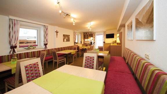 A cozy interior with wooden tables and colorful benches. Large windows provide plenty of daylight and a welcoming atmosphere. - Pension Pitze - Sölden