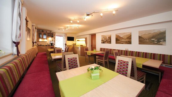 A cozy dining area with colorful seats and wooden tables. The walls are decorated with pictures and windows that create a warm atmosphere. - Pension Pitze - Sölden