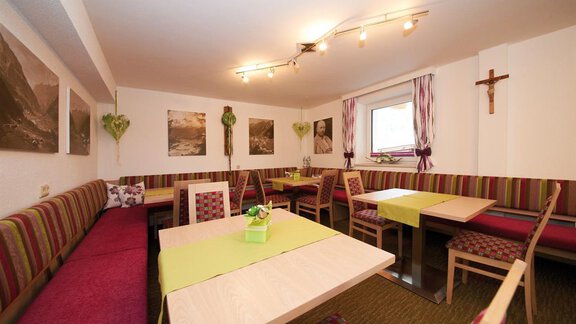 A cozy restaurant with colorful benches and tables. Pictures of landscapes hang on the walls, and there is a small decorative cross. - Pension Pitze - Sölden