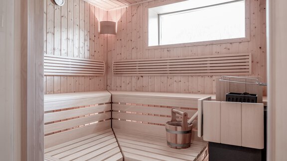 A modern wooden sauna with benches and a sauna stone stove. A large window provides natural light. - Soelden Lounge - Sölden