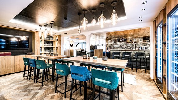 A modern dining room with a long wooden table and blue chairs. The walls are painted in warm tones and there is stylish lighting. - Sonnalp Residences - Sölden