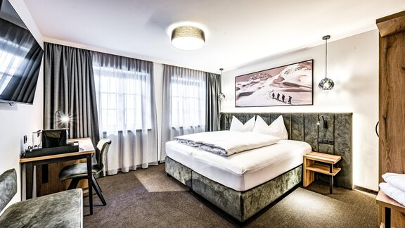 A modern hotel room with a comfortable double bed and a television. Large windows provide plenty of daylight and a pleasant atmosphere. - Sonnalp Residences - Sölden