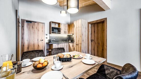 A modern kitchen corner with a dining table, dinnerware, and food. The space has wood details and pleasant lighting. - Sonnalp Residences - Sölden