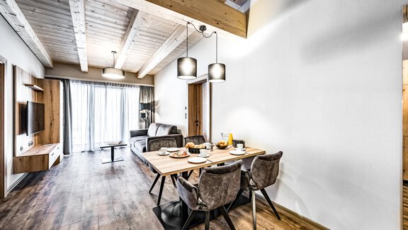 A modern living room with a dining table and cozy chairs. Large windows let in plenty of light and create a bright, inviting atmosphere. - Sonnalp Residences - Sölden