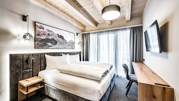 A modern room with a comfortable double bed and a large window. The decor features a light wooden ceiling and stylish decorative elements. - Sonnalp Residences - Sölden