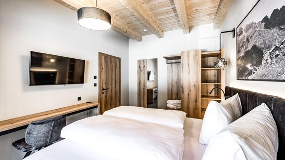 A modern bedroom with a large bed and wooden ceiling. The decor is simple, with a television and a desk. - Sonnalp Residences - Sölden