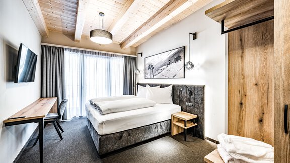 A modern bedroom with a comfortable double bed and a cozy wooden ceiling. The room features large windows for plenty of daylight and an outdoor view. - Sonnalp Residences - Sölden