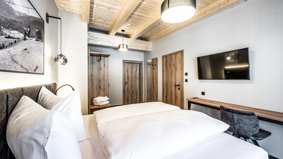 A modern bedroom with two beds and bright pillows. The walls are tastefully designed, and there is a television as well as a desk. - Sonnalp Residences - Sölden