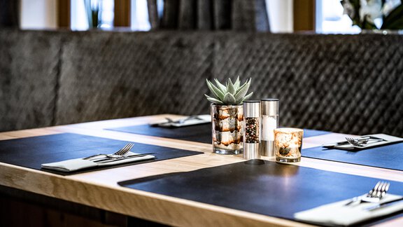 An elegant table with black placemats and cutlery. In the center are decorative candles and a plant. - Sonnalp Residences - Sölden