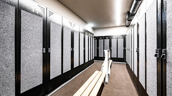 A modern changing room with gray lockers and a wooden bench. The walls are light and well-lit. - Sonnalp Residences - Sölden