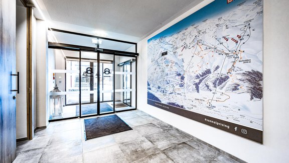 A modern entrance area with large glass doors and a clear site plan on the wall. The floor is tiled in gray, and the room feels bright and inviting. - Sonnalp Residences - Sölden