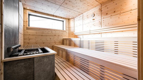 A modern sauna with wooden paneling and two benches. Natural light falls through a window, creating a relaxing atmosphere. - Sonnalp Residences - Sölden