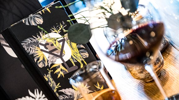 A stylish table with a book and wine glasses. Decorative plants are visible in the background. - Sonnalp Residences - Sölden