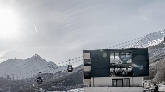 A modern building in the mountains with a cable car in the foreground. The landscape is wintry and offers a view of snow-covered peaks. - THE VIEW by Regina - Sölden