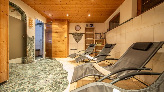 A cozy wellness area with loungers and a wooden ceiling. The floor is made of natural stones, and there is access to a sauna area. - Toni's Ferienheim - Sölden
