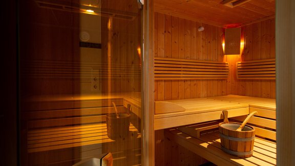 A cozy sauna made of light wood with gentle lighting. Inside, there is a wooden barrel and a shovel. - Toni's Ferienheim - Sölden