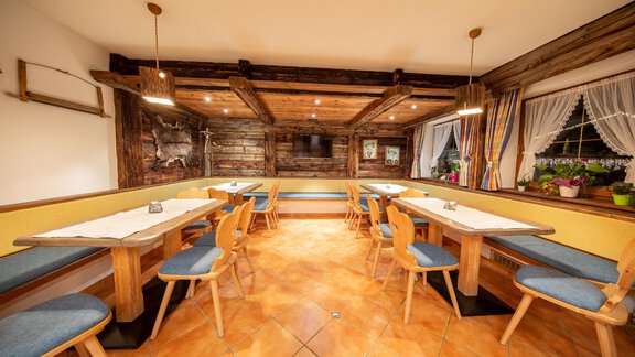 A cozy restaurant area with wooden walls and wooden furniture. The tables are brightly decorated and there is plenty of natural light. - Toni's Ferienheim - Sölden