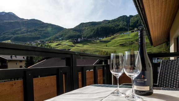 A beautiful balcony with a view of green mountains and houses. On the table are two glasses and a bottle of sparkling wine. - Top Apart Daniela - Sölden