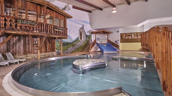 A modern swimming area with a round pool and wooden decor. In the background, a slide and a picturesque mural are visible. - Top Apart Daniela - Sölden