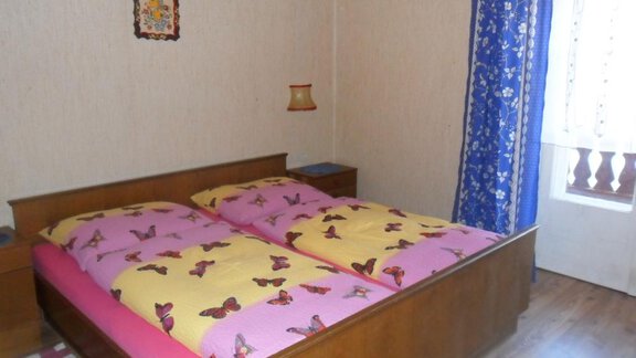 A cozy bedroom with a double bed and colorful bedspreads. The room has a window with curtains and a wooden wardrobe. - Appt. Garni Anny - Vent
