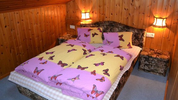 A cozy bedroom with a double bed and colorful blankets. The walls are made of wood, and there is soft lighting from two bedside lamps. - Appt. Garni Anny - Vent