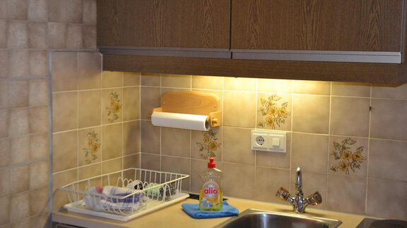 A small kitchen with wooden cabinets and a sink. On the countertop are dishes and a soap dispenser. - Appt. Garni Anny - Vent