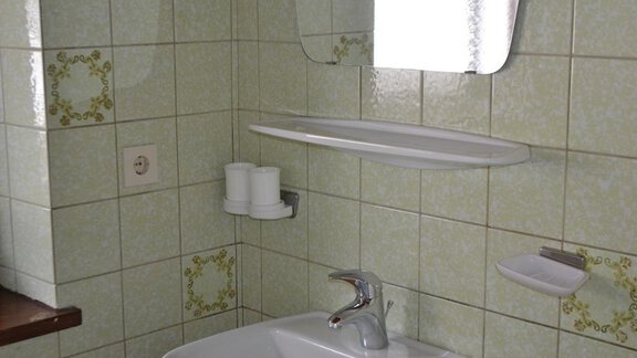A simple bathroom with a white sink and a mirror. The walls are adorned with green tiles and decorative elements. - Appt. Garni Anny - Vent