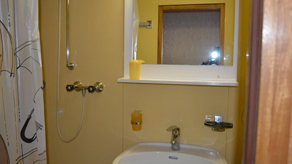 A simple bathroom with a shower and a white sink. The walls are painted yellow and there is a small mirror above. - Appt. Garni Anny - Vent