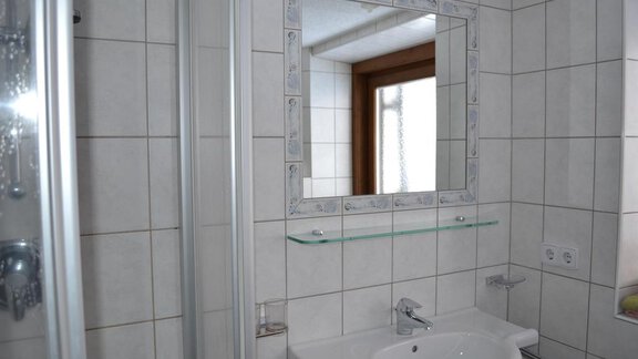 A modern bathroom with a shower and a sink. The large mirror reflects the light and creates a bright atmosphere. - Appt. Garni Anny - Vent
