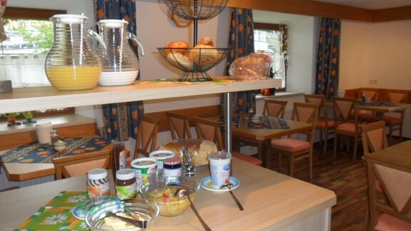 A breakfast area with a buffet offering various foods like jam, fruit, and bread. The tables are decorated in a rustic style, and the atmosphere is friendly and inviting. - Appt. Garni Anny - Vent