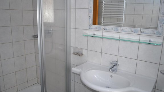 A modern bathroom with a shower and a sink. The walls are tiled with light tiles. - Appt. Garni Anny - Vent