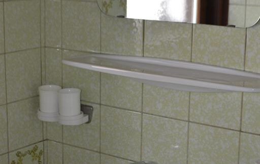 A simple bathroom with a sink and a mirror. The walls are tiled with light green tiles. - Appt. Garni Anny - Vent