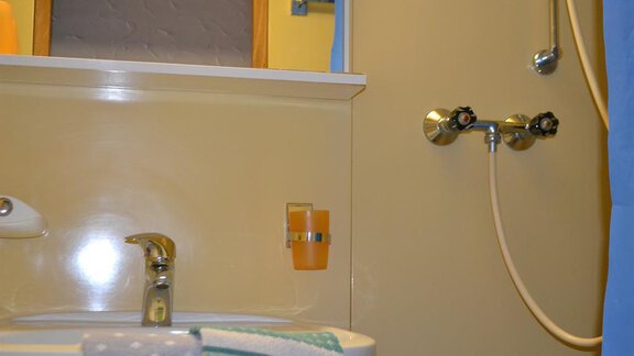 A bathroom with a sink and a shower. The walls are painted in light yellow, and there are some towels and a cup in orange. - Appt. Garni Anny - Vent