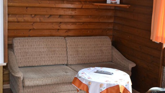 A cozy living area with a beige sofa and a table. The walls are made of wood and there are tight curtains. - Appt. Garni Anny - Vent