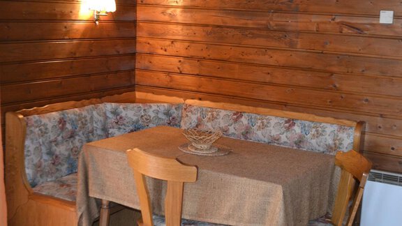 A cozy dining area with a padded seating corner and a wooden table. The walls are made of dark wood, and a lamp provides warm light. - Appt. Garni Anny - Vent