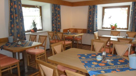 A cozy dining room with wooden chairs and tables. The walls are painted light and decorated with colorful curtains. - Appt. Garni Anny - Vent