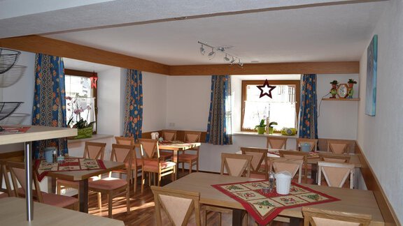 An inviting dining area with bright tables and chairs. The windows are decorated with colorful curtains, and a cozy atmosphere is enhanced by the plants. - Appt. Garni Anny - Vent