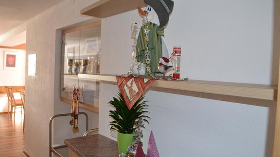 A decorative wooden shelf with a snowman and various small decorative elements. In the background, a dining area and some trophies can be seen. - Appt. Garni Anny - Vent