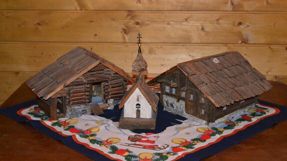 A handmade model of traditional wooden houses and a church on a colorful tablecloth. The scene evokes alpine architecture and rural life. - Appt. Garni Anny - Vent