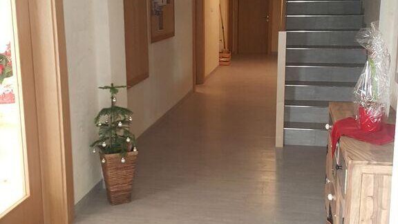 A bright hallway with a staircase and decorative elements. On the left side, there is a small pot with a plant, and a rug lies on the floor. - Gästehaus Soldanella - Vent