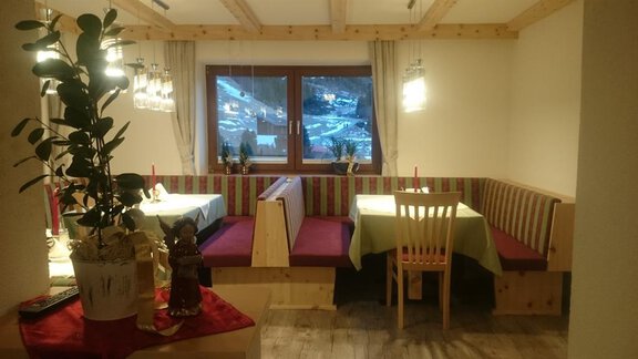 A cozy restaurant with wooden furniture and a warm atmosphere. The tables are set for an inviting meal, and a window offers a view outside. - Gästehaus Soldanella - Vent