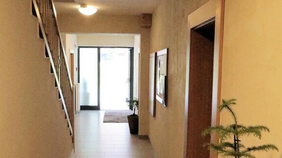 A bright hallway with a wooden staircase and modern tile look. On the right, there is a small plant on a piece of furniture. - Gästehaus Soldanella - Vent