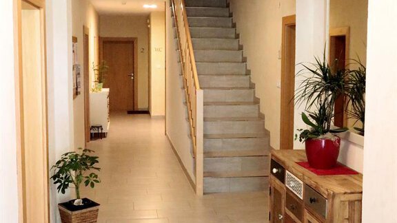 A bright hallway with stairs and a wooden cabinet. Plants and an inviting atmosphere create a friendly ambiance. - Gästehaus Soldanella - Vent