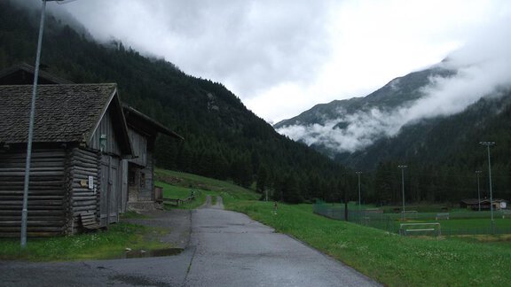 A quiet landscape with a narrow path leading through green meadows. In the background, forested mountains and clouds can be seen. - Gasthof Brückenwirt - Zwieselstein