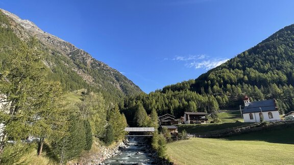 A clear river flows through a green landscape, surrounded by mountains. The sky is blue and radiant. - Landhaus Rosenhof - Zwieselstein