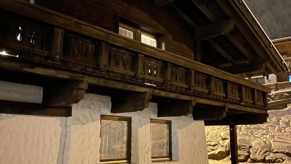An old wooden house with a balcony and a snow-covered ground. It is nighttime and the building appears cozy and inviting. - Landhaus Rosenhof - Zwieselstein