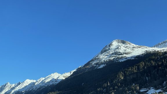 A snow-covered mountain landscape under a clear blue sky. In the foreground, some cottages and a small village can be seen. - Landhaus Rosenhof - Zwieselstein