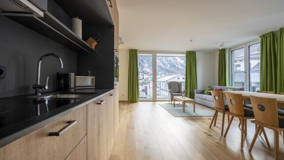 A modern apartment with an open kitchen and a cozy living area. Large windows provide a view of the surrounding mountains. - Zwieselstein-Apart De Luxe - Zwieselstein