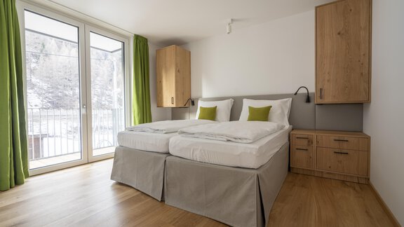 A modern bedroom with two beds and bright, friendly colors. Large windows offer a view outside and let in plenty of light. - Zwieselstein-Apart De Luxe - Zwieselstein